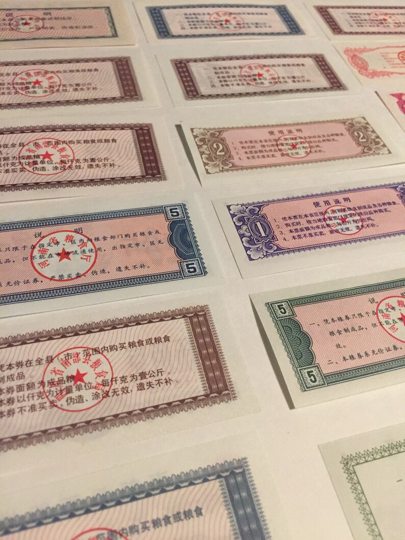 May include: A collection of vintage Chinese food ration coupons. The coupons are printed on paper and feature red and blue borders. The coupons are in denominations of 2 and 5. The coupons have Chinese text and a red star.