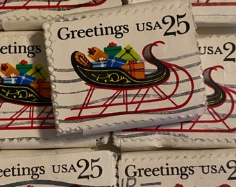 May include: A collection of vintage postage stamps featuring a Christmas sleigh filled with gifts. The stamps read "Greetings USA 25" and have a red and black sleigh design with a white background.