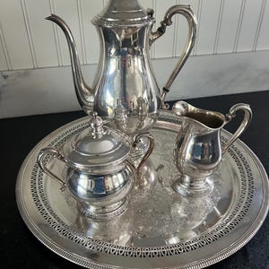 Puede incluir: Un juego de té de plata con tetera, jarra de crema, azucarero y bandeja. El juego tiene un diseño ornamentado y está en excelentes condiciones.