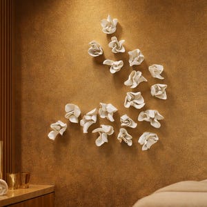 Pode incluir: Interior de spa com decoração de parede floral abstrata branca. Toalhas brancas enroladas, velas e detalhes dourados criam um ambiente relaxante. A parede tem um acabamento texturizado e quente.
