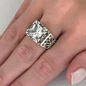 May include: A silver ring with a large, clear square-shaped gemstone set in a filigree design.