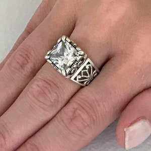 May include: A silver ring with a large, clear square-shaped gemstone set in a filigree design.