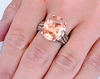 May include: A silver ring with a large, peach-colored gemstone. The ring has a wide band with intricate details.
