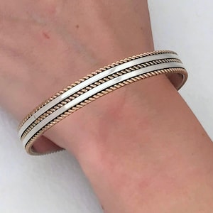 May include: A silver and gold bangle bracelet with a braided design.