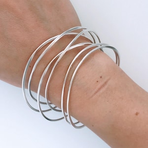 May include: A set of silver bangles stacked on a person's wrist. The bangles are thin and have a smooth, polished finish.