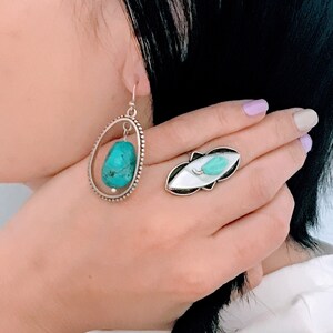 May include: A pair of silver earrings with turquoise stones and a silver ring with a turquoise stone. The ring is on a finger and the earrings are hanging from the ear.