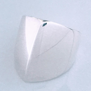 May include: A polished silver ring featuring a wide, tapered band that comes to a distinct, sharp point at the center. The metal surface is smooth and reflective, showcasing a clean, geometric design with a high-shine finish throughout the piece.