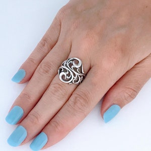 May include: A silver ring with a delicate, ornate design. The ring is on a hand with light blue nail polish.