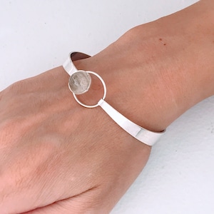 May include: A silver bangle bracelet with a round, clear stone set in a circle.