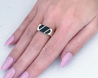 May include: A silver ring with a black rectangular stone set in the center. The stone has three diagonal lines etched into it.