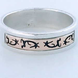 May include: A silver band ring with a rose gold inlay and black etched designs.