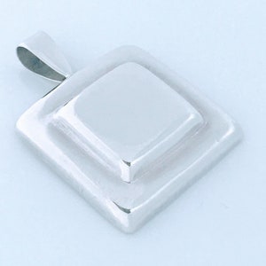 May include: A silver pendant with a square design. The pendant has a raised square in the center.
