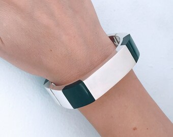 May include: A silver and green geometric bangle bracelet. The bracelet is made of silver and has a green enamel inlay.