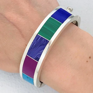 May include: A silver bangle bracelet with a colorful inlay of turquoise, purple, green, and blue stones.