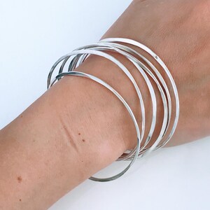 May include: A set of silver bangles stacked on a person's wrist. The bangles are thin and have a hammered finish.