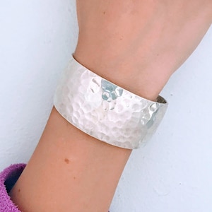 May include: A silver hammered bangle bracelet. The bracelet is wide and has a textured surface.
