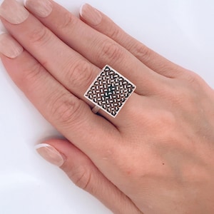 May include: A silver ring with a square-shaped design featuring a woven pattern.