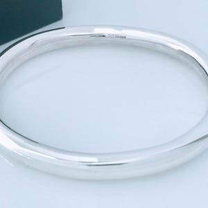 May include: A polished, silver-colored bangle bracelet. The bracelet is a thick, rounded band with a smooth, reflective surface. The text "925 MEXICO" is stamped on the inside of the bracelet. The bracelet is displayed on a white surface.