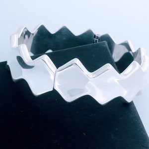 May include: A silver bracelet with a geometric design. The bracelet is made of a series of interlocking, slightly rounded, diamond-shaped links.