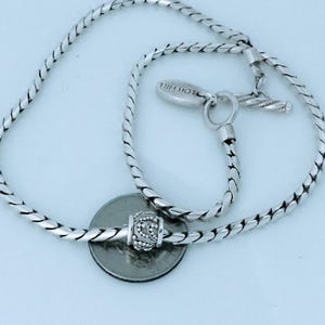 May include: A silver necklace with a braided chain design. The necklace features a decorative bead and a toggle clasp. The brand name "LOIS HILL" is engraved on the clasp. A quarter is placed next to the necklace for size reference.