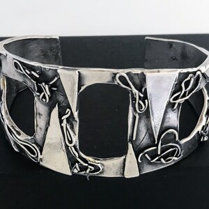 May include: A silver cuff bracelet with a geometric design. The bracelet has a textured surface and is made of metal.