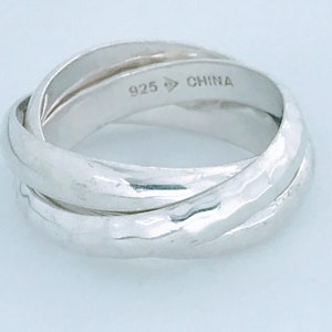 May include: A silver-colored triple band ring featuring an interlocking design with a hammered texture. The interior of the band is clearly engraved with the text 925 and CHINA, indicating the metal composition and country of origin for this jewelry.