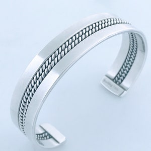 May include: A silver bangle bracelet with a rope-like design on the top and bottom edges.