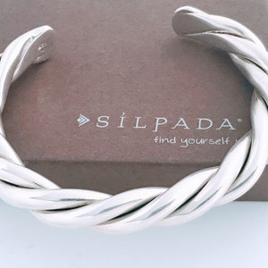 May include: A silver twisted bangle bracelet with the brand name "SÍLPADA" and the tagline "find yourself" on the box.