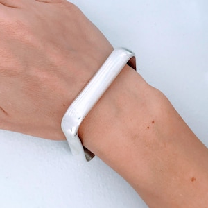 May include: A silver bangle bracelet with a square shape and rounded edges.