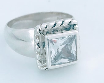 May include: A silver ring with a square-shaped clear stone set in a decorative silver frame.