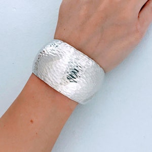 May include: A silver hammered cuff bracelet with a textured surface.