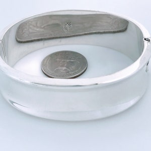 May include: A silver bangle bracelet with a smooth, rounded surface. The bracelet is about the size of a quarter.
