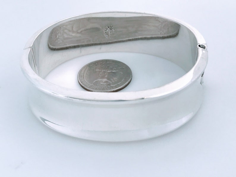 May include: A silver bangle bracelet with a smooth, rounded surface. The bracelet is about the size of a quarter.