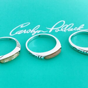 May include: Three silver rings with a light brown inlay on a turquoise background. The rings are all different designs. The background has the signature "Carolyn Pollack" written in cursive.