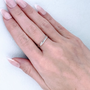 May include: A close-up of a hand wearing a thin silver band ring. The hand has long, oval-shaped fingernails with a white tip.