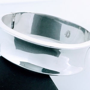 May include: A silver bangle bracelet with a smooth, curved design. The bracelet is marked "925 Mexico".