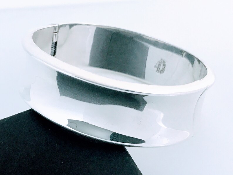 May include: A silver bangle bracelet with a smooth, curved design. The bracelet is marked "925 Mexico".