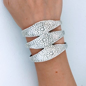 May include: A silver-colored cuff bracelet with a textured, dotted pattern. The bracelet wraps around the wrist in three sections, creating a layered effect. The jewelry is displayed on a light background.
