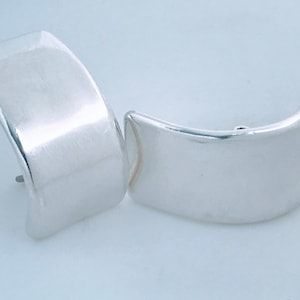 May include: A pair of silver earrings with a curved, rectangular shape. The earrings are smooth and have a polished finish.