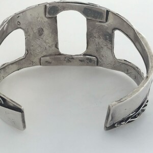 May include: Silver bracelet with a cutout design. The bracelet is open on one side and has a textured surface.