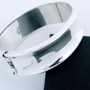 May include: A silver hinged bangle bracelet with a smooth, rounded surface.