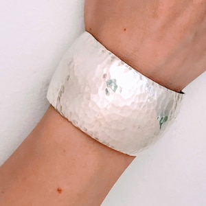 May include: A silver hammered cuff bracelet. The bracelet is wide and has a rounded shape.