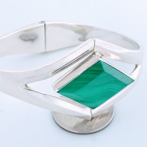 May include: A silver bangle bracelet with a green malachite stone set in the center. The stone is a rectangular shape with rounded corners and has a swirling pattern.