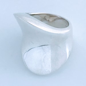 May include: A silver ring with a smooth, organic shape. The ring is wide and has a rounded, asymmetrical design.
