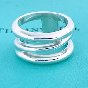 May include: A silver ring with three bands that are intertwined. The ring is on a turquoise blue background.