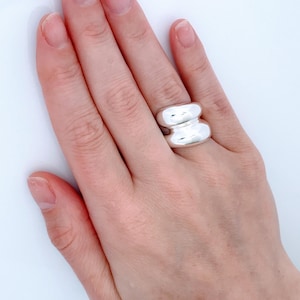 May include: A silver ring with a smooth, rounded design. The ring is thick and has a wide band.
