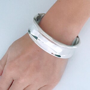 May include: A silver bangle bracelet with a smooth, rounded surface.