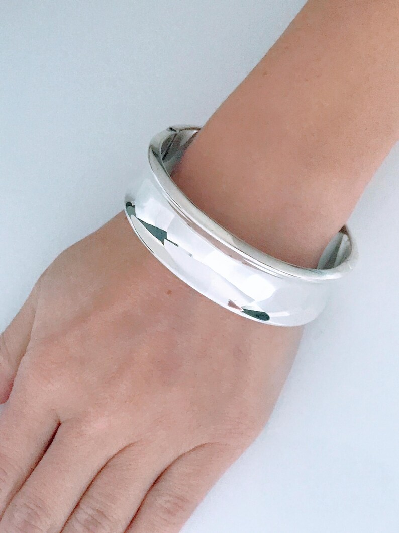 May include: A silver bangle bracelet with a smooth, rounded surface.