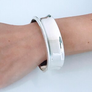 May include: A silver bangle bracelet with a wide, rounded band.