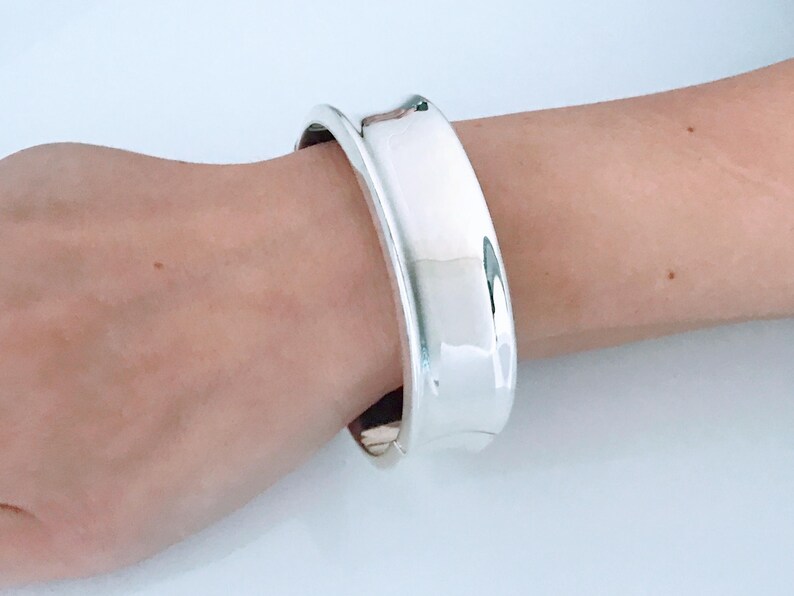 May include: A silver bangle bracelet with a wide, rounded band.